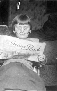 Girl's newspaper, 1920s, A child with glasses reads a newspaper with interest, sitting comfortably