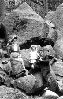 Couple with 1 child hiking, 1910, A family on a rocky outcrop in hiking clothes, holding hats and