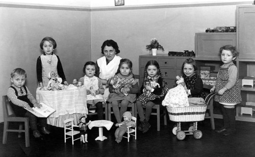 Kindergarten group toys, 1930s, children with woman in the room, playing with dolls and toys at a