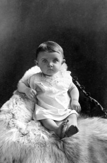 Baby sitting on polar bear fur, 1910, A baby sits on a fur, looking directly into the camera,