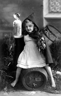 Girl drinking beer, ca. 1920, A girl with a hood is sitting on a barrel, holding an object in a