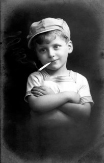 Boy smoking, 1920, Black and white photo of a boy with cap and cigarette in a casual pose,