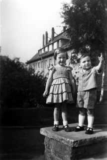 Boy showing girl something, 1920, Two children on a piece of wall outdoors with a building in the