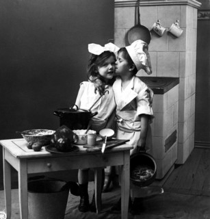 Boy kissing girl in kitchen, 1920, Two children in a kitchen setting with pots and crockery, one