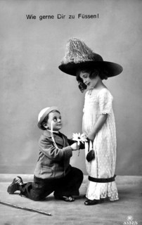 Boy kneeling in front of girl, 1910, A boy with flowers kneeling in front of a girl in a big hat,