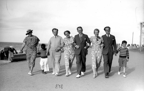 Family outing on the beach promenade, 1930s, A group of people stroll along the beach in elegant