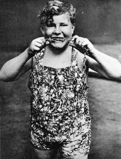 Child biting chains, 1910, A boy in a suit shows strength by pulling a chain and smiling,