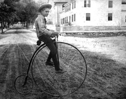 Boy on a penny-farthing, 1910s bicycle, Boy on an antique bicycle on a sandy street in a