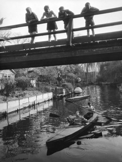 Four children on a bridge, 1930s, Children standing on a bridge while teenagers paddle underneath