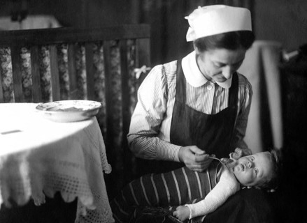 Nanny feeding child, 20s, 1920s, A woman lovingly feeds a baby in a domestic, historical setting,