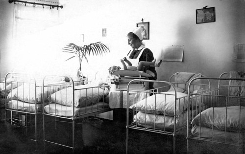 Beds Midwife cradling child, 1930s, Nurse caring for a baby in a room with several cots, Historical