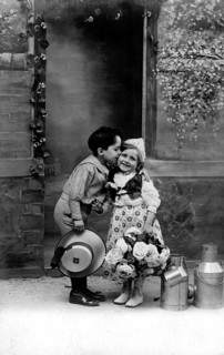 Boy kisses girl, 1920s, A boy kisses a girl on the cheek, surrounded by flowers and pewter cans,