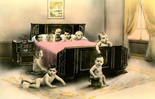 Nine babies in a bed, 1920s, Several babies crawling curiously around a large bed in a room,