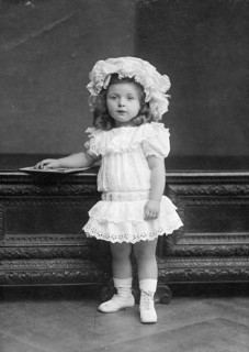 Little girl in dress, 1920s, Little girl in lace dress and hat posing in front of piece of