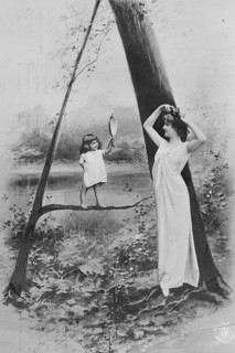 Looking in the mirror, 1920s, A woman and a child holding a hand mirror pose in front of a tree in