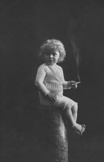 Child smoking, 1920s, A child in historical clothing sits on a pedestal and holds a cigarette in