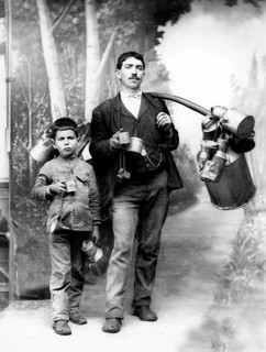 Milkman with apprentice, 1910s, adult and child with pewter cans, standing as father-son pair,