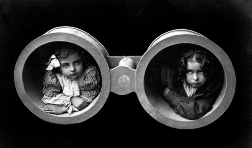 Two girls in binoculars, 1920s, Two children looking through oversized binoculars in a black and