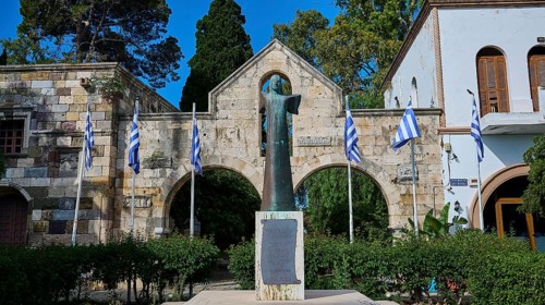 Statue surrounded by Greek flags and historical architecture in the garden, Kos Town, Venetian City