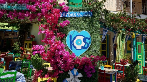 Colourfully decorated taverna with flowers and heart-shaped kos sign, sunny atmosphere, Platia