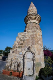 Historic fountain next to a stone tower under a clear blue sky, Eski Cami, Minaret, Kos Town, Kos,