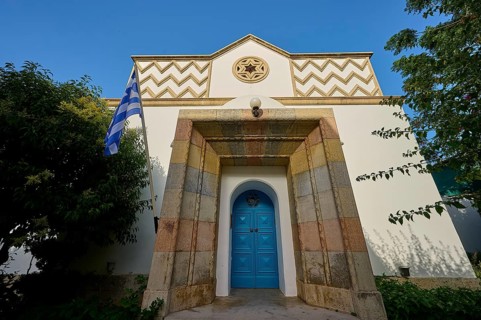 Greek architecture with turquoise door and flag on bright, sunny background, Synagogue, Kos Town,
