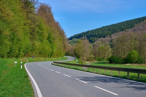 Winding country road leads through a green, wooded landscape under a clear sky, spring, Burgsinn,