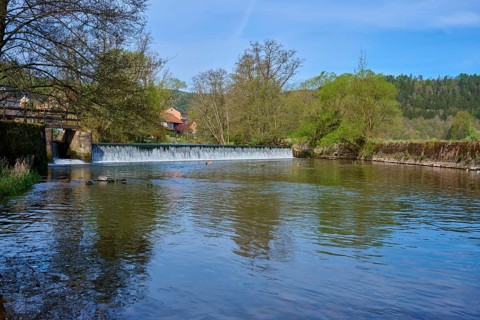 Calm river water in front of a dam wall, surrounded by green nature and blue sky, spring, Obersinn,
