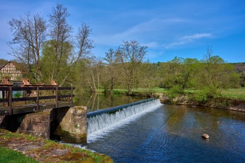A weir in the river leads to a small waterfall, surrounded by trees, spring, Obersinn, Sinntal,