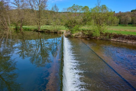 Small dam wall with falling water and reflection of the trees in the river, spring, Obersinn,