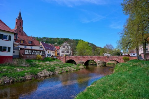 Picturesque small town view with river Saale, bridge and half-timbered houses under blue sky,