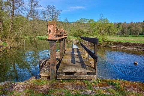 Wooden footbridge over a body of water in a natural setting with trees in the background, spring,