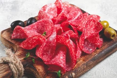 Sliced salami sausage, on a wooden chopping board, decorated with olives and herbs, close-up, no