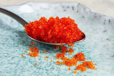 A spoon with orange flying fish caviar, Tobiko, on a light blue plate, caviar for rolls and sushi,