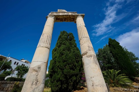 ©Udo Rein, Ancient stone columns in front of a bright blue sky and surrounded by tall trees, Temple