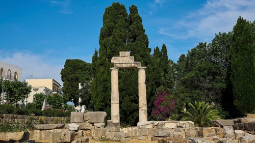 ©Udo Rein, Column ruins in a landscape of trees and blue sky with buildings in the background,