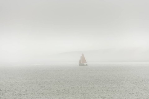 A sailing boat is travelling on the ocean on a cloudy day. The sky is overhanging and the water is