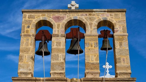 Church of Agios Ioannis Prodromos, Triple bell tower made of stone with blue sky in the background,