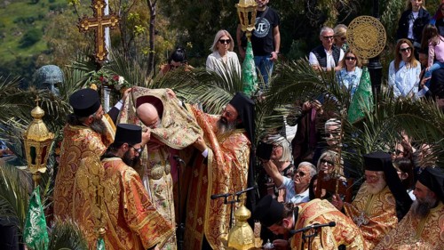 Priests standing under a cross during an outdoor religious ceremony surrounded by worshippers and