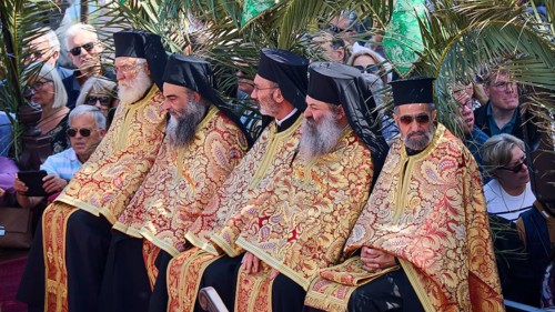 Several priests in golden robes sitting next to each other at an outdoor ceremony, surrounded by