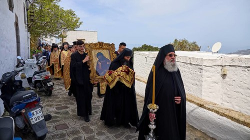 Priests in black robes and icon bearers walk along a wall during a religious procession, Orthodox