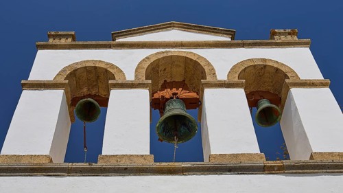 Cross-domed church of Panagia Diasosousan, white bell tower with three bells against a clear sky,