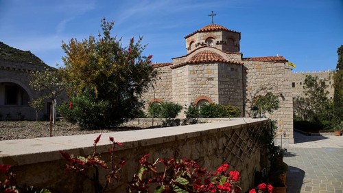 Stone church with tiled roof, surrounded by a blooming garden under a blue sky, woman's monastery,