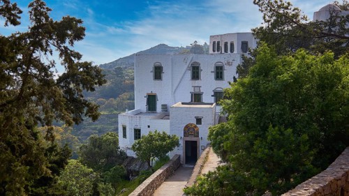 White monastery building surrounded by dense vegetation and a sunny sky, Monastery of the
