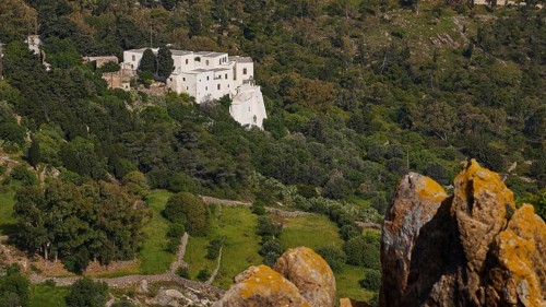 White building from a distance in a wooded landscape with rocks in the foreground, Monastery of the