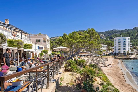 Outdoors restaurant on a terrace with tourist sitting in the sunshine and looking at the seascape