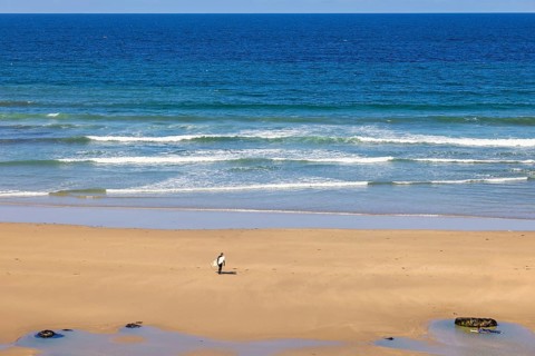 Man with a surfboard walking on a sand beach by the sea a sunny summer day, Crozon peninsula,