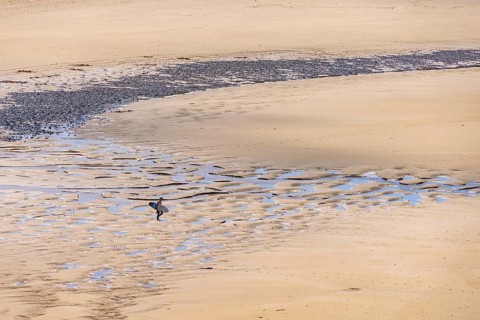 Man with a surfboard walking on a sand beach on the way to the sea a sunny summer day, Crozon