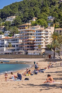 People sunbathing on a sandy beach at a tourist resort with houses close to the shore at the