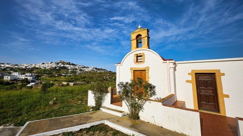 White chapel with wooden door and cross, surrounded by green nature, chapel south of the Chora,